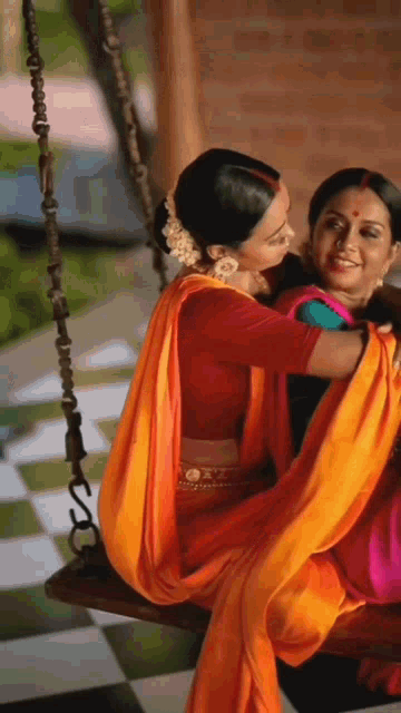 two women are sitting on a swing and one of them is wearing a red top