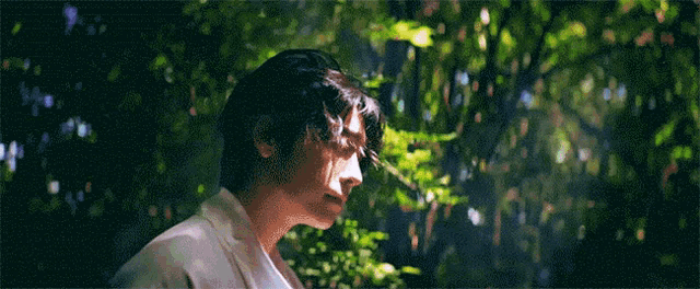 a man in a white shirt is standing in a forest with trees behind him .