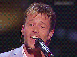 a man in a suit singing into a microphone while playing a guitar