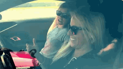 two women wearing sunglasses are sitting in a car and one of them is giving a thumbs up