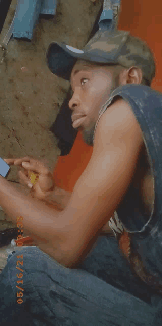 a man wearing a hat is sitting down and looking at his cell phone