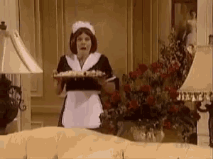 a woman dressed as a maid is holding a tray of food .