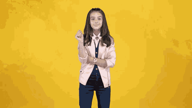 a young girl wearing a pink jacket and blue pants waves her hand