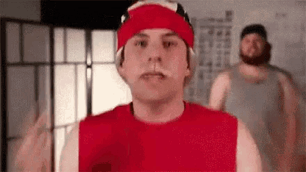 a man wearing a red headband and a red tank top is standing in front of a mirror .