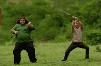 two men are standing in a field holding swords in their hands .