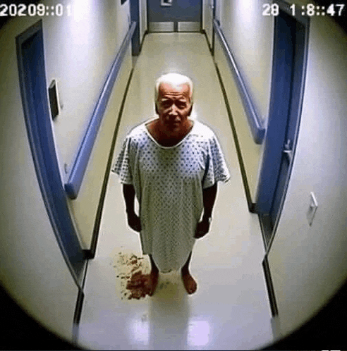 an elderly man in a hospital gown is standing in a hallway with blood on the floor .
