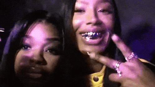 a couple of women standing next to each other with their mouths open and giving a peace sign .
