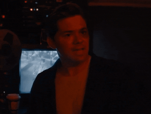 a man in a dark room with a cup of coffee in front of a monitor