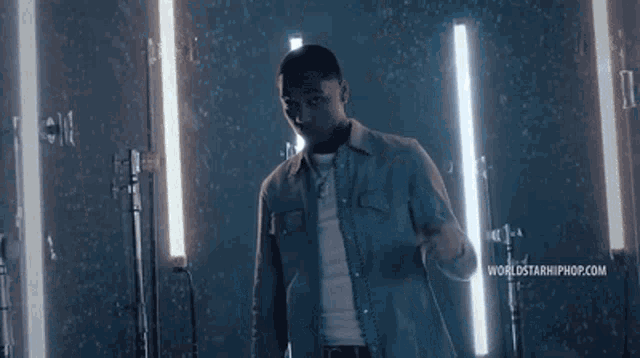 a man in a denim jacket is standing in front of a mirror and holding a microphone .