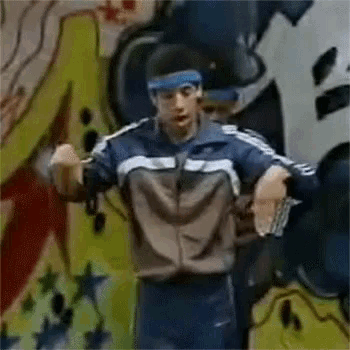 a man wearing a headband and a jacket is standing in front of a wall with graffiti on it .
