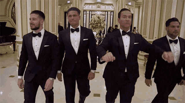 a group of men in tuxedos are walking down a hallway holding hands