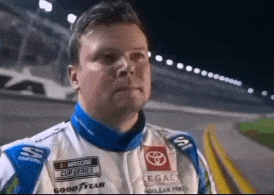 a man is standing on a race track wearing a racing suit .