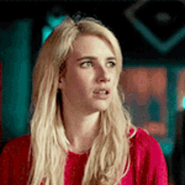 a woman with blonde hair is wearing a red sweater and looking at the camera .