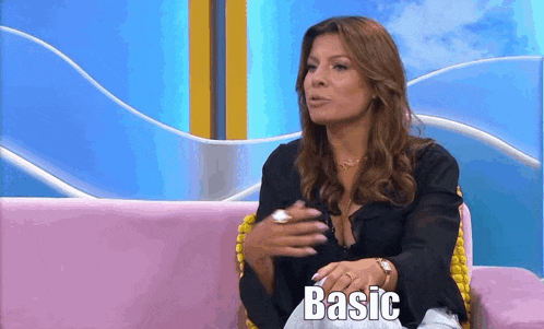 a woman is sitting on a pink couch and the word basic is on the screen behind her