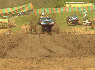 a jeep is driving through a muddy field with a green and orange tent in the background