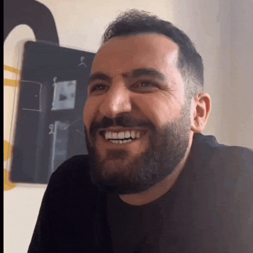 a man with a beard is smiling in front of a chalkboard