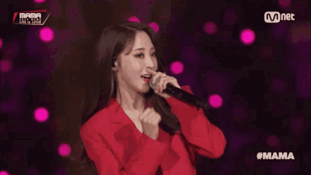 a woman in a red jacket singing into a microphone with #mama written on the bottom