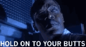 a man with glasses is looking at the camera with the words hold on to your butts below him .