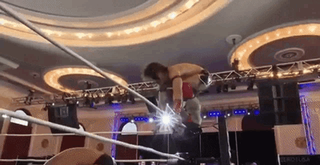 a wrestling match is taking place in a large room with a ceiling that has a lot of lights .