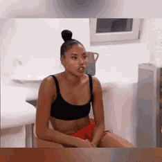 a woman in a black bra and red shorts is sitting on a chair
