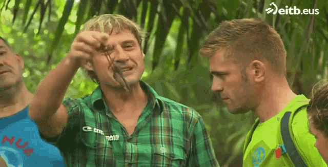 a man in a green plaid shirt is holding a snake