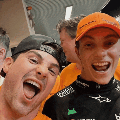 two men are posing for a picture and one of them is wearing an orange hat that says " petronas "