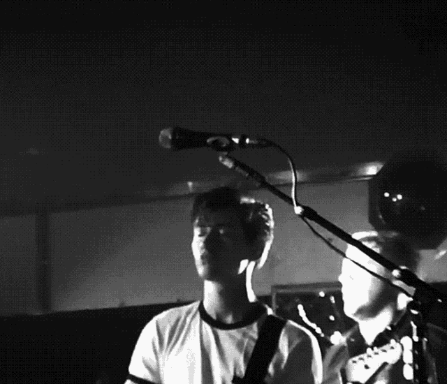 a man singing into a microphone with another man playing a guitar in the background