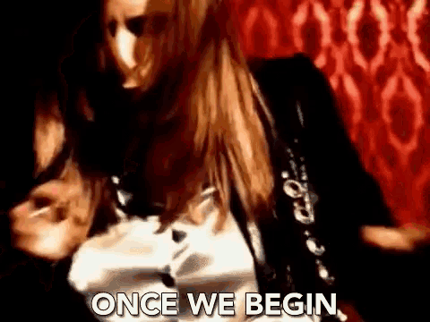 a woman is dancing in front of a red wall and the words `` once we begin '' are written on the screen .