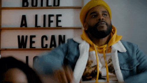 a man in a yellow hat stands in front of a sign that says build a life we can