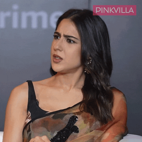 a woman wearing a black top and a floral saree with a pinkvilla logo behind her