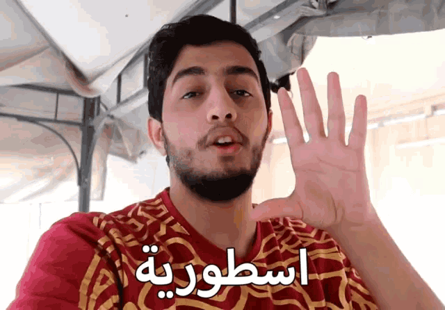 a man wearing a red and gold shirt with arabic writing behind him