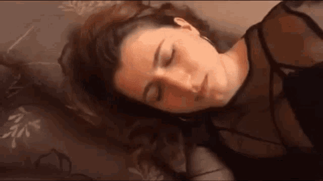 a woman is laying on a bed with her eyes closed and her hair is blowing in the wind .