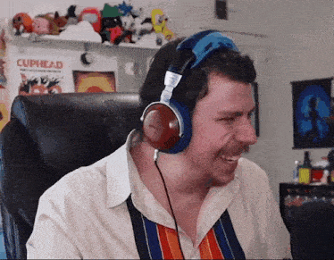 a man wearing headphones is smiling in front of a poster that says cuphead