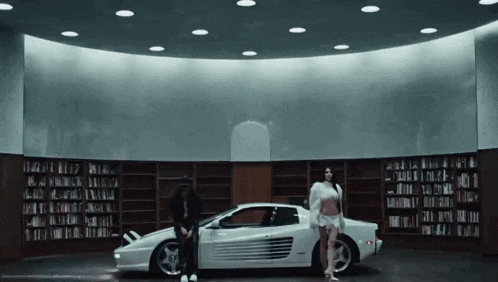 a man and a woman are standing next to a white sports car in a library