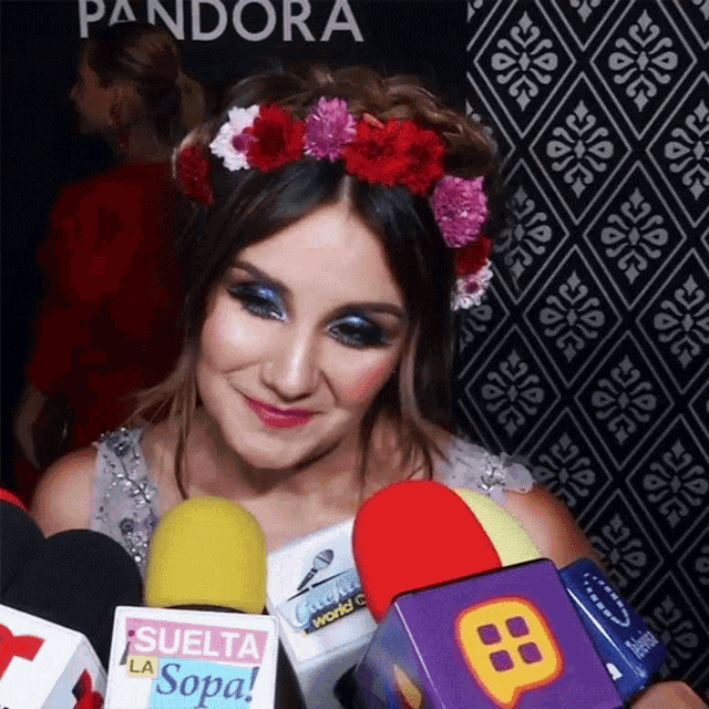 a woman wearing a flower crown is surrounded by microphones and a suelta la sopa sign