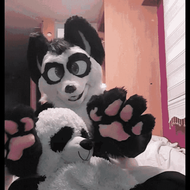 a black and white furry animal holding a stuffed panda