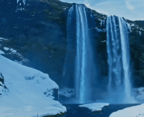 a waterfall is surrounded by snow covered mountains