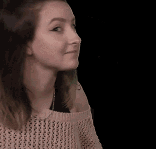 a woman is wearing a pink sweater and looking to the side on a black background .