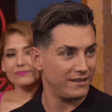a close up of a man 's face with a woman in the background behind him