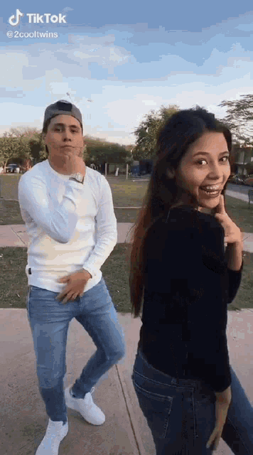 a man and a woman are standing next to each other on a sidewalk in a park .