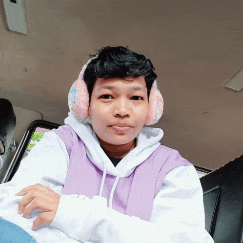 a man wearing ear muffs and a purple hoodie looks at the camera