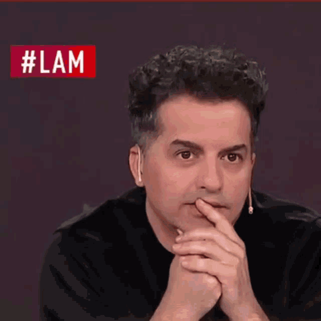 a man is smiling in front of a red sign that says #lam
