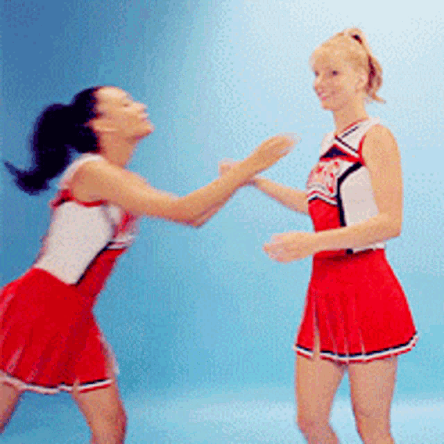 two cheerleaders wearing red skirts are dancing together