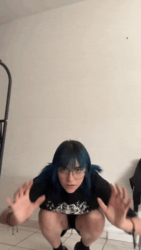 a girl with blue hair is squatting down with her hands outstretched .