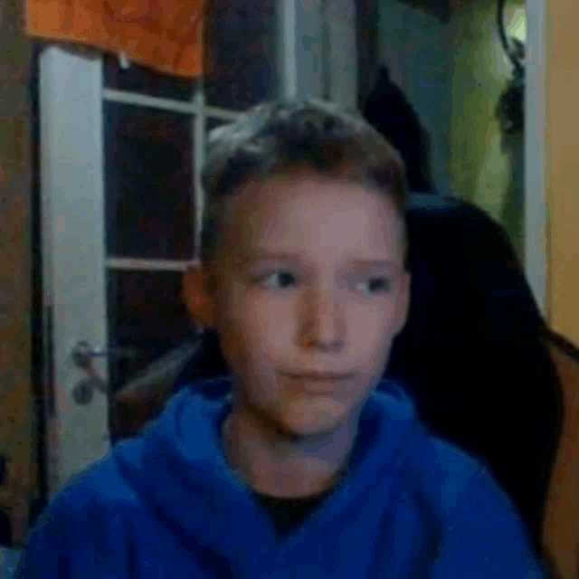 a young boy in a blue hoodie is making a funny face while looking at the camera .