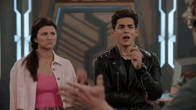 a man in a black leather jacket stands next to a woman in a pink top