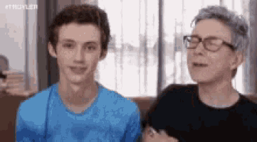 a man and a boy are sitting next to each other on a couch . the boy is wearing a blue shirt .