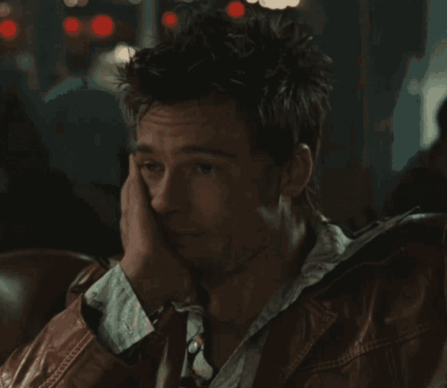 a man in a leather jacket is sitting down with his hand on his face