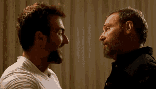 two men are looking at each other and laughing while standing next to each other .