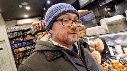 a man wearing glasses and a blue hat stands in front of a display of buffalo wing